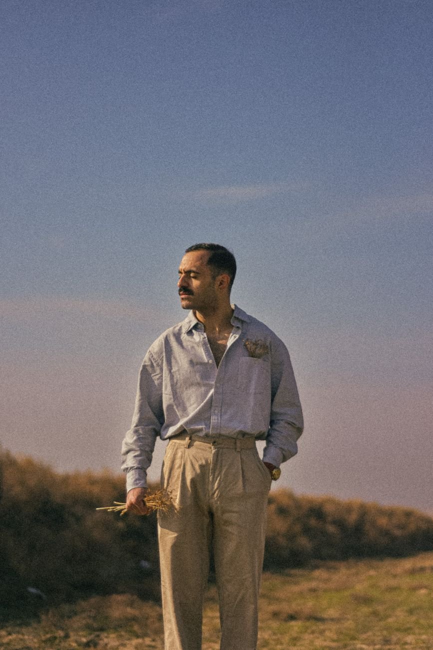 Man wearing beige trousers and a shirt standing outdoors in warm natural light