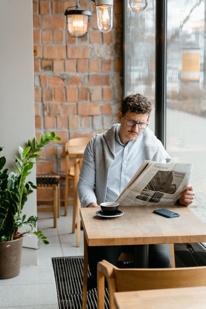 Man reading a newspaper at a rustic coffee shop, relaxed and well-dressed